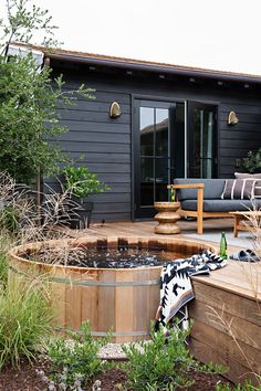 a wooden hot tub sitting in the middle of a garden next to a patio area