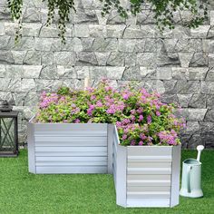 two planters sitting on the grass next to a stone wall with purple flowers in it