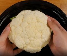 two hands holding a piece of cauliflower on a black plate