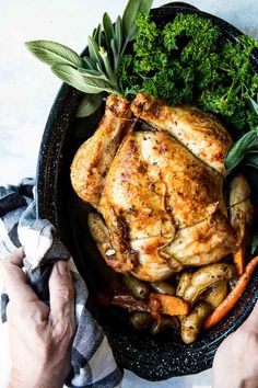 a person holding a knife over a roasting pan filled with chicken and vegetables