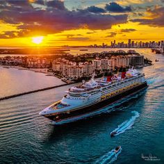 a cruise ship sailing in the ocean at sunset with city skylines in the background