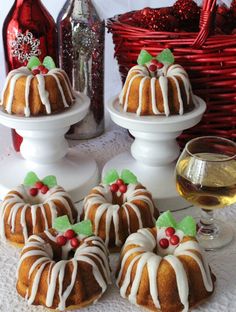 small bundt cakes with white icing and holly decorations on them next to wine glasses