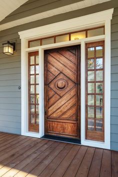 a wooden door sitting on the side of a gray house next to a light fixture