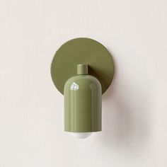 a green light fixture mounted on the side of a white wall next to a round object