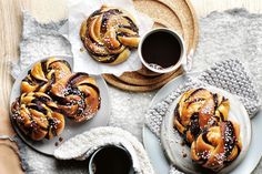 two plates filled with cinnamon buns next to cups of coffee and napkins on a table