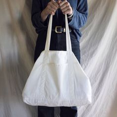 a person holding a white bag in front of a white wall with a cell phone