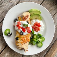 an enchilada with sour cream, black olives and tomatoes on a white plate