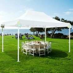 a large white tent set up on top of a lush green field next to the ocean