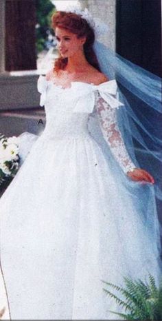 a woman in a white wedding gown and veil walking down the street with her hand on her hip