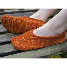 a woman's feet in orange knitted slippers sitting on a wooden bench