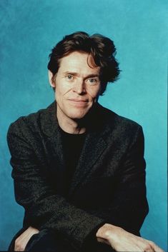 a man sitting in front of a blue background with his arms crossed and looking at the camera