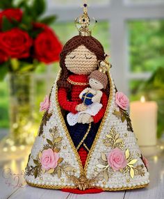 a crocheted doll holding a baby in her arms on a table with roses