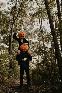 a woman carrying two pumpkins on her shoulders in the woods with trees and leaves