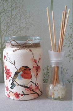 a glass jar with a bird painted on it next to two reeds and a vase