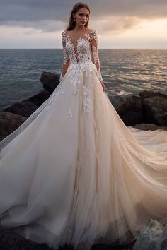 a woman in a wedding dress standing on rocks near the ocean