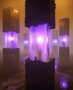 an illuminated fountain in the middle of a foggy area with purple lights on it