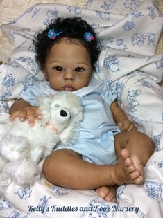 a baby girl holding a stuffed animal on top of a white bed covered in blue sheets