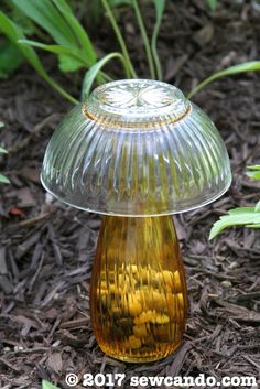 a yellow glass lamp sitting on the ground next to some grass and flowers in the background