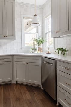 a kitchen with white cabinets and wood floors is pictured in this image, there are plants on the window sill