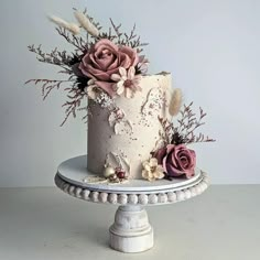 a white cake with pink flowers and feathers on the top is sitting on a pedestal