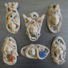 five ceramic wall hangings with faces and ornaments on the top one is painted white