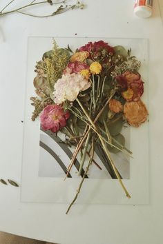 an arrangement of flowers is displayed on a white table with scissors and glue next to it