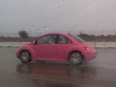 a pink car driving down a wet road