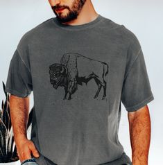 Bison Tee Shirt, Mens Buffalo Tshirt The Comfort Colors C1717 100% Ring Spun Cotton T-Shirt is very appropriately-named. All colors are inspired by nature and have a perfect lived-in, weathered look. Shirts are sent through a unique dyeing process that makes them incredibly soft and long-lasting. Each piece is soft-washed 50 times before making its way to you! Stitched at the collar, armhole, sleeves and bottom hem for ultimate durability, you will notice the density and quality of this shirt, b Perfect Live, Mens Tee Shirts, Dyeing Process, Inspired By Nature, Fabric Softener, Twill Tape, Favorite Shirts, Comfort Colors, Buffalo