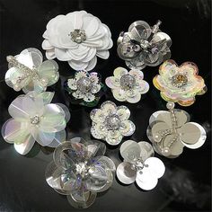 there are many different types of flower brooches on the black table with white flowers