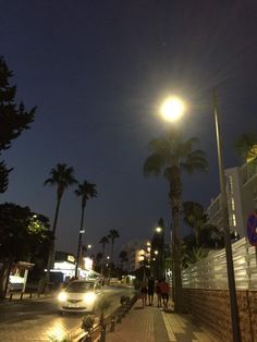 people walking down the sidewalk at night with palm trees and street lights in the background