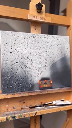 a car is driving down the road in the rain on an easel with some paintbrushes next to it