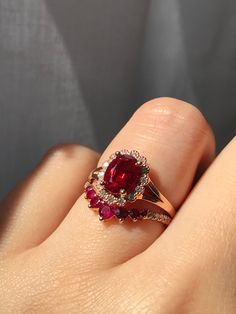 a close up of a person's hand holding a ring with a red stone