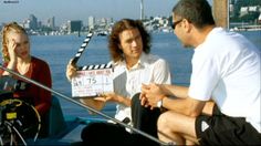 three people sitting on a boat with a movie clapper in front of them and the water behind them