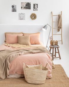 a bed with pink sheets and pillows in a bedroom next to a wooden chair, ladder and pictures on the wall