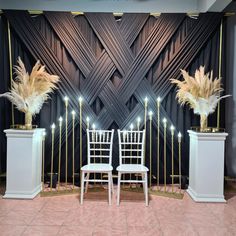 two white chairs sitting next to each other in front of a black wall with gold accents