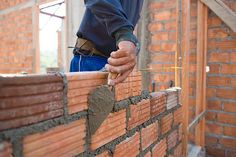 a brick wall being built by a man with a hammer in his hand and another person working on it