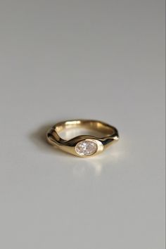 a gold ring with a single diamond on the top, sitting on a white surface