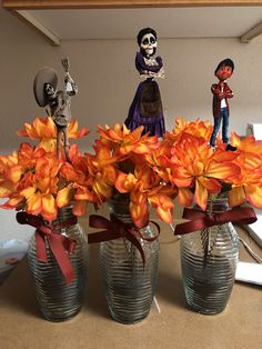 three vases filled with orange flowers and skeleton figurines on top of a table