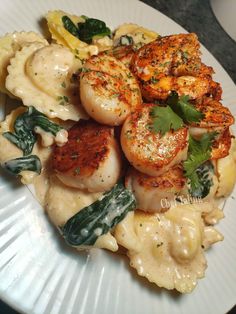 a white plate topped with pasta covered in scallops and garnishes