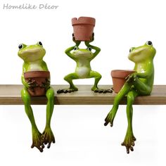 three green frogs are sitting on a shelf and one is holding a flower pot