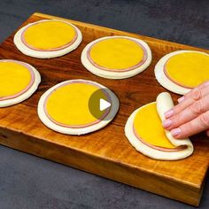 a person is making mini sandwiches on a wooden board with yellow icing and white frosting