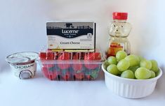 grapes, yogurt and other fruit are arranged on a white countertop next to a jar of cream cheese