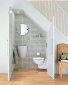 a white toilet sitting next to a wooden floor under a stair case in a bathroom