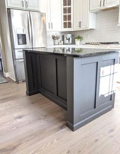 a large kitchen island in the middle of a room with white cabinets and stainless steel appliances