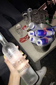 a person holding up a bottle of vodka next to some glasses and bottles on a table