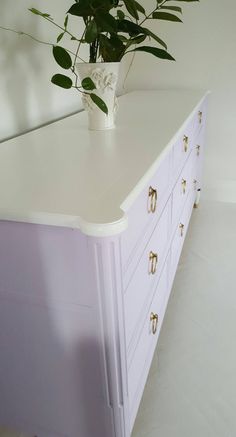 a plant is sitting on top of a white dresser with brass handles and knobs