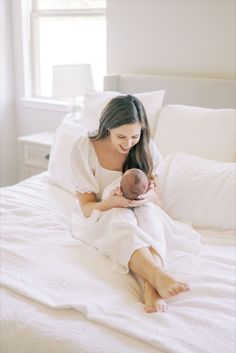 a woman holding a baby in her arms while laying on top of a white bed