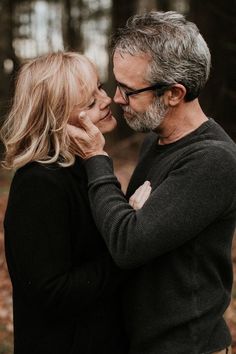 an older man and woman embracing in the woods