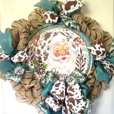 a wreath with a santa clause on it hanging from the front door, decorated with burlap and green leaves