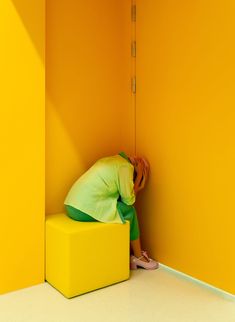 a person sitting on top of a yellow bench in a room with an orange wall